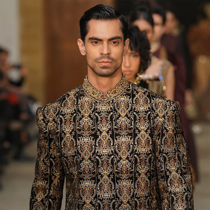 Black velvet sherwani with zari embroidery, paired with black dhoti shalwar.