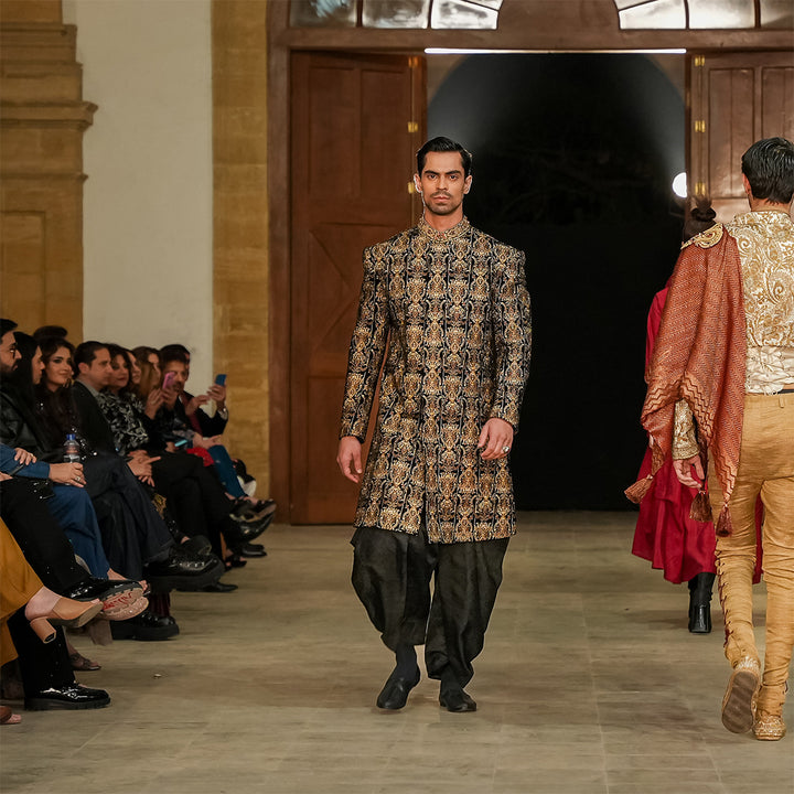 Black velvet sherwani with zari embroidery, paired with black dhoti shalwar.